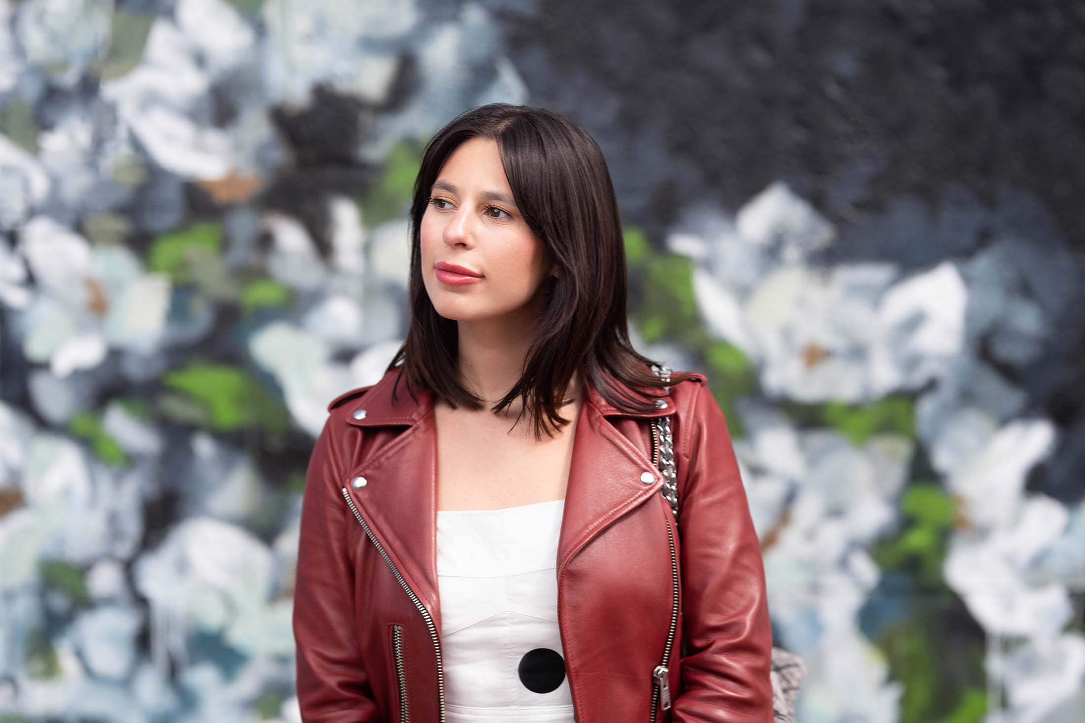 a woman wearing a red leather jacket in front of a flower wall.