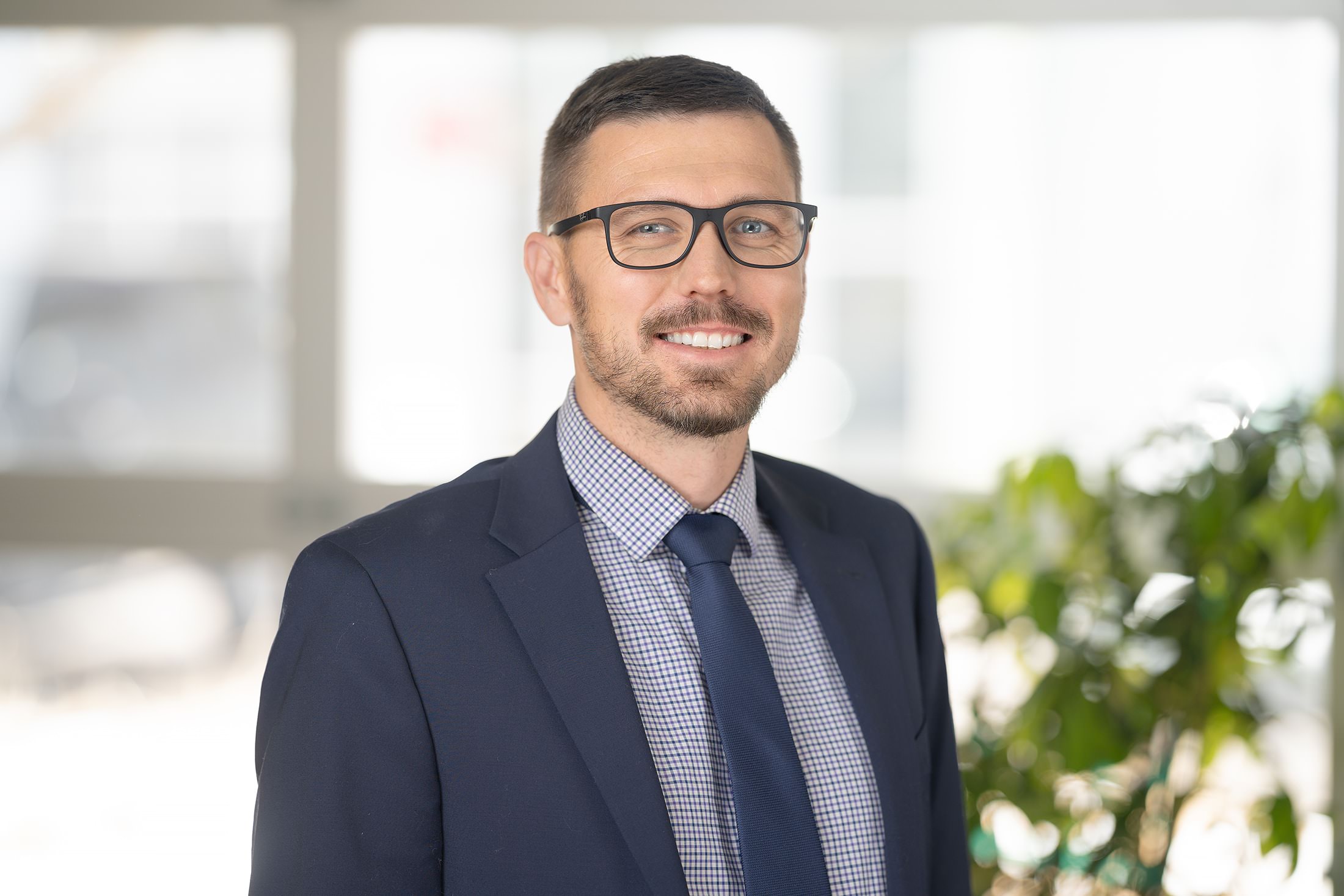 a man in a suit and tie smiles in front of a plant.