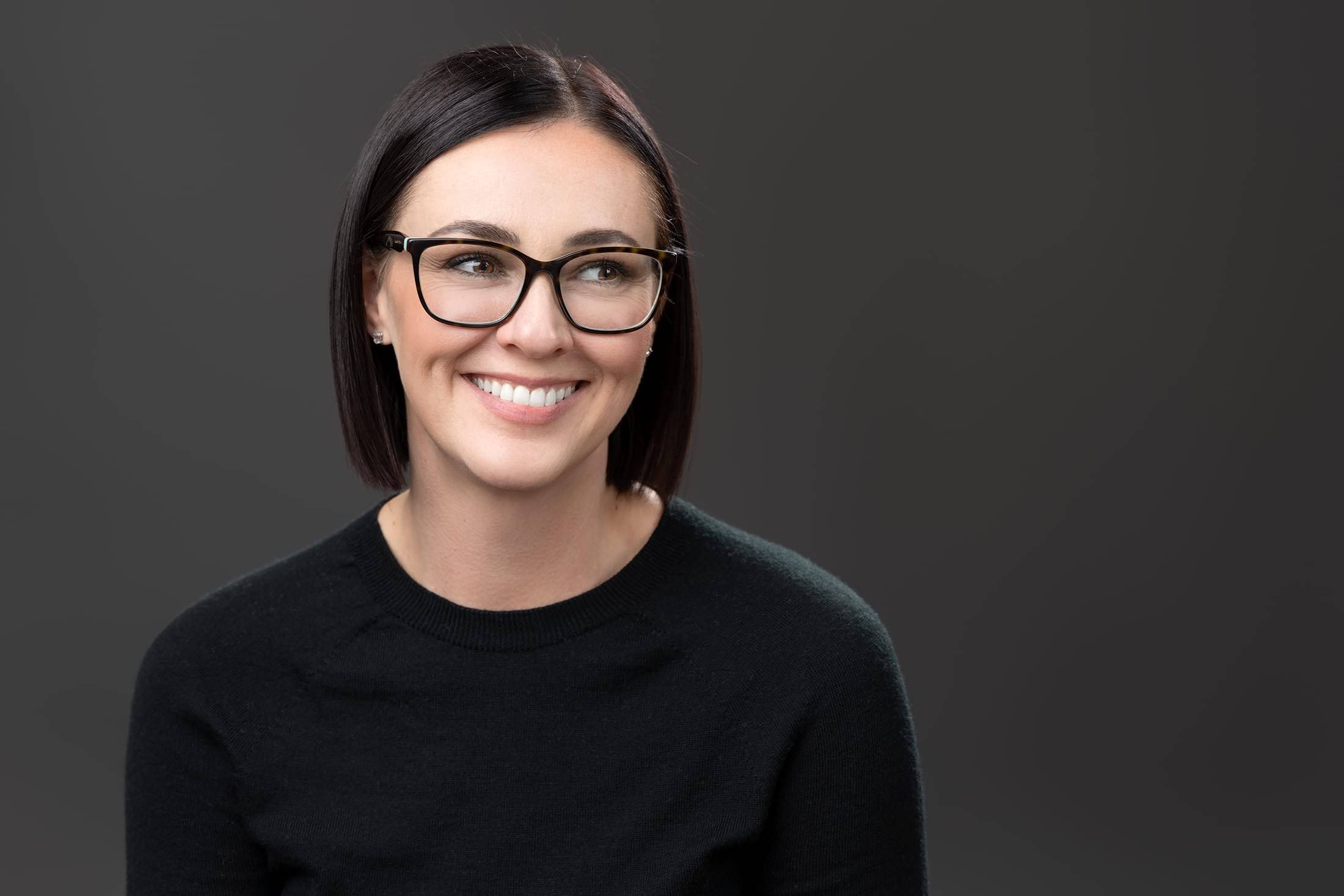 a smiling woman wearing glasses on a grey background.