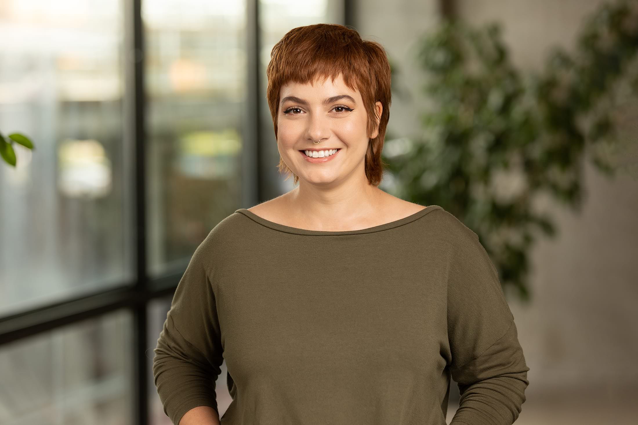 a smiling woman in a green shirt standing in front of a window.