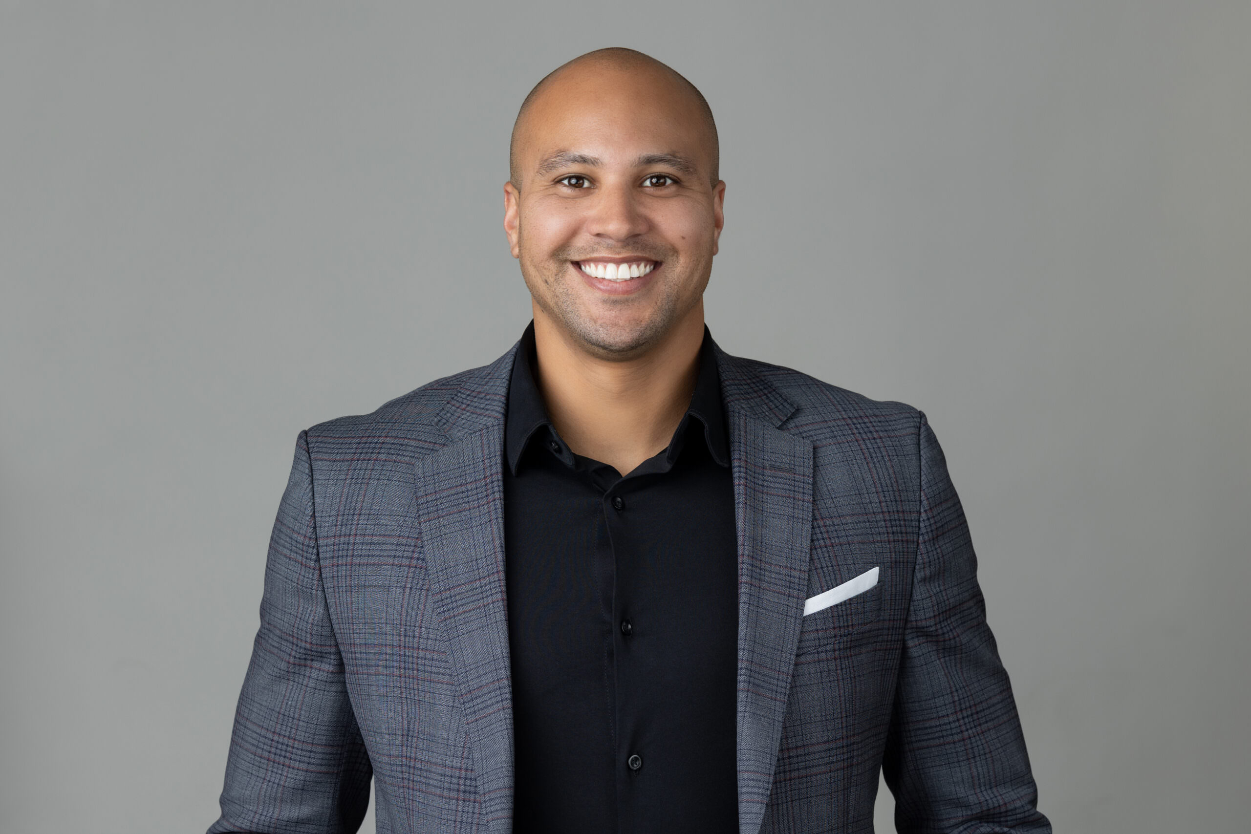 A well-lit bald man in a suit smiling for the camera, conveying a positive message.