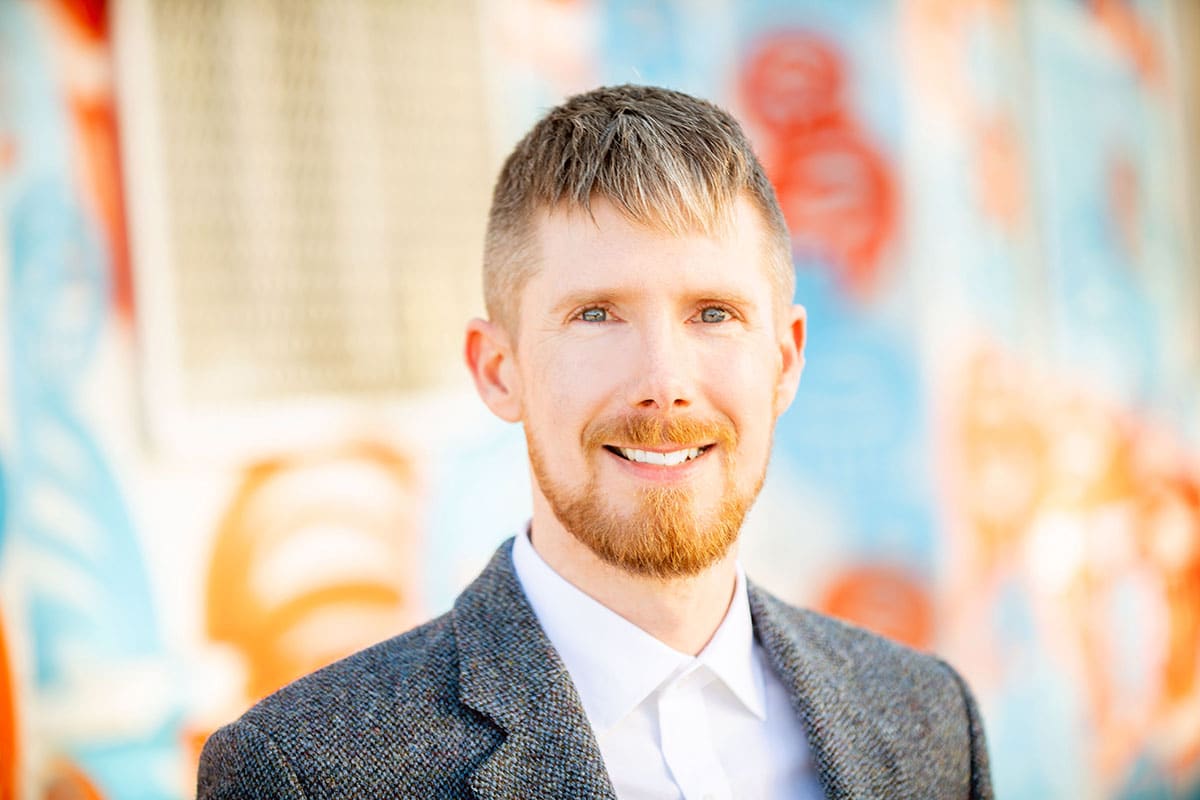 a man with a beard smiling in front of a colorful wall.