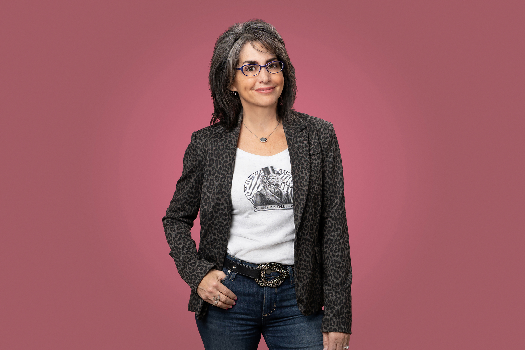 A woman in jeans and a t-shirt striking a pose against a vibrant pink background.