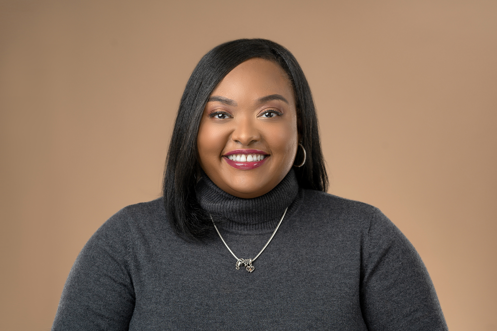 a black woman with a headshot wearing a gray turtleneck and silver necklace.