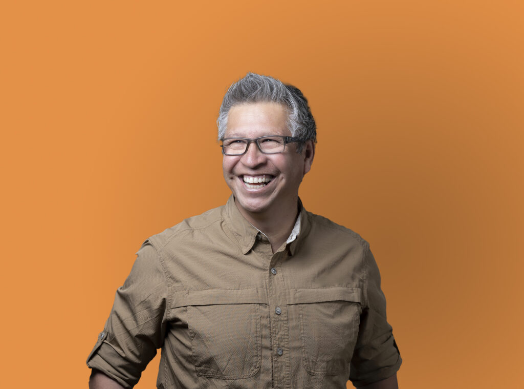 A man's personal branding photography with a smiling pose against an orange background.