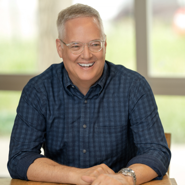 headshot of an elderly man with glasses in a blue checkered shirt