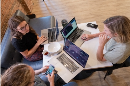 four women sitting around a table with laptops.