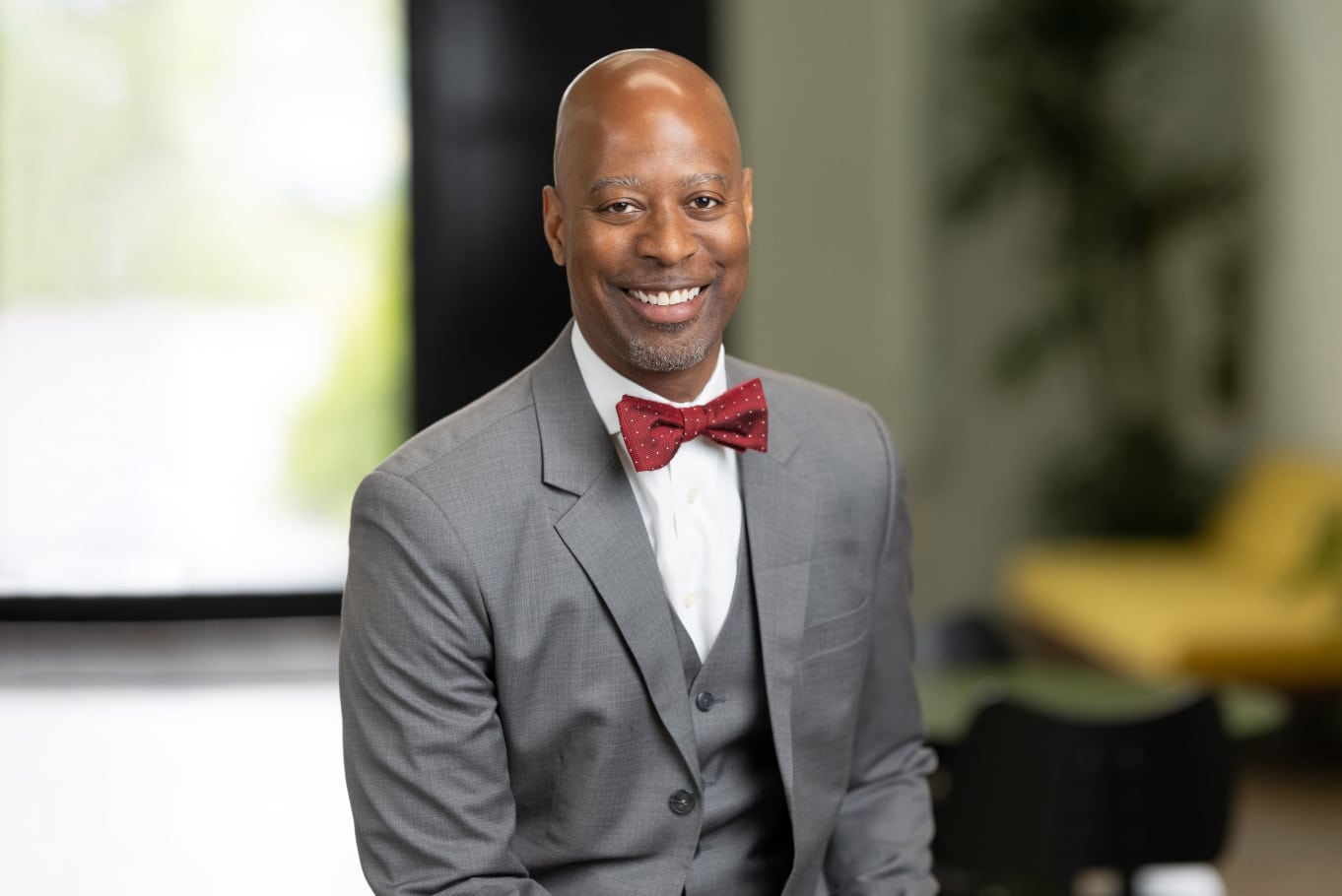 a black man in a suit and red bow tie smiling.