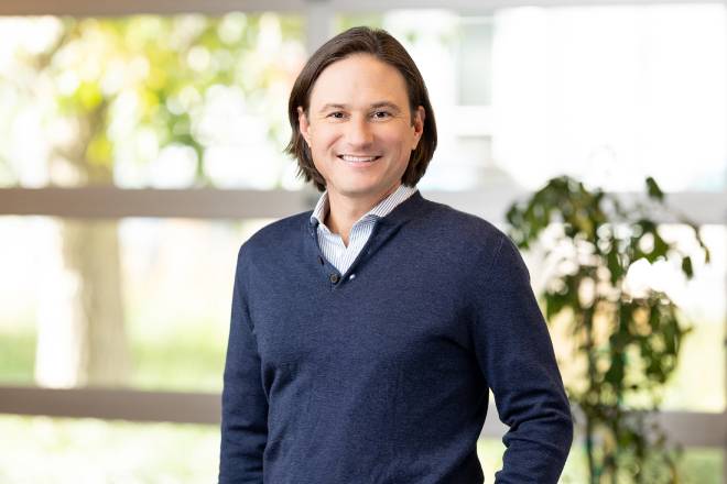 a man in a blue sweater posing for individual headshots in front of a window.