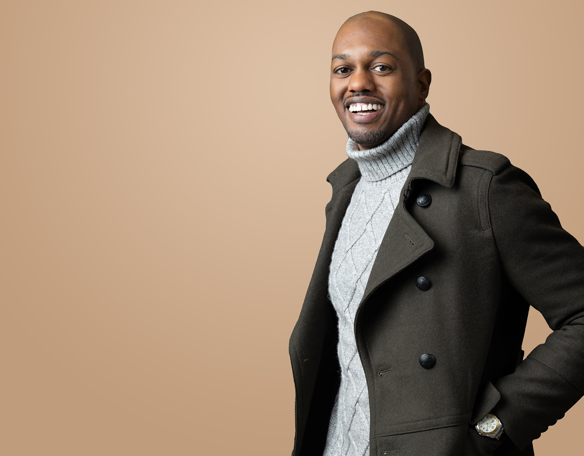 a black man in company matching program apparel posing on a beige background.