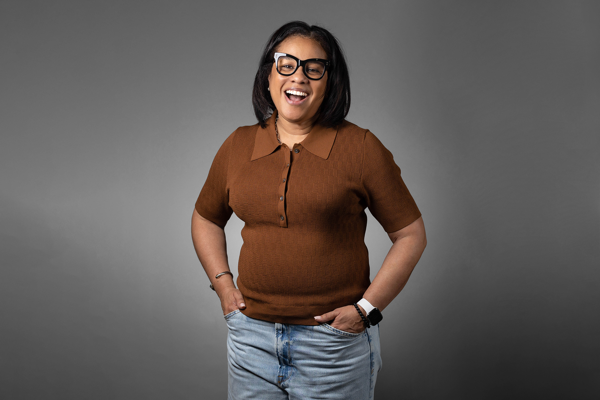 A woman wearing glasses and jeans posing for a corporate headshot.