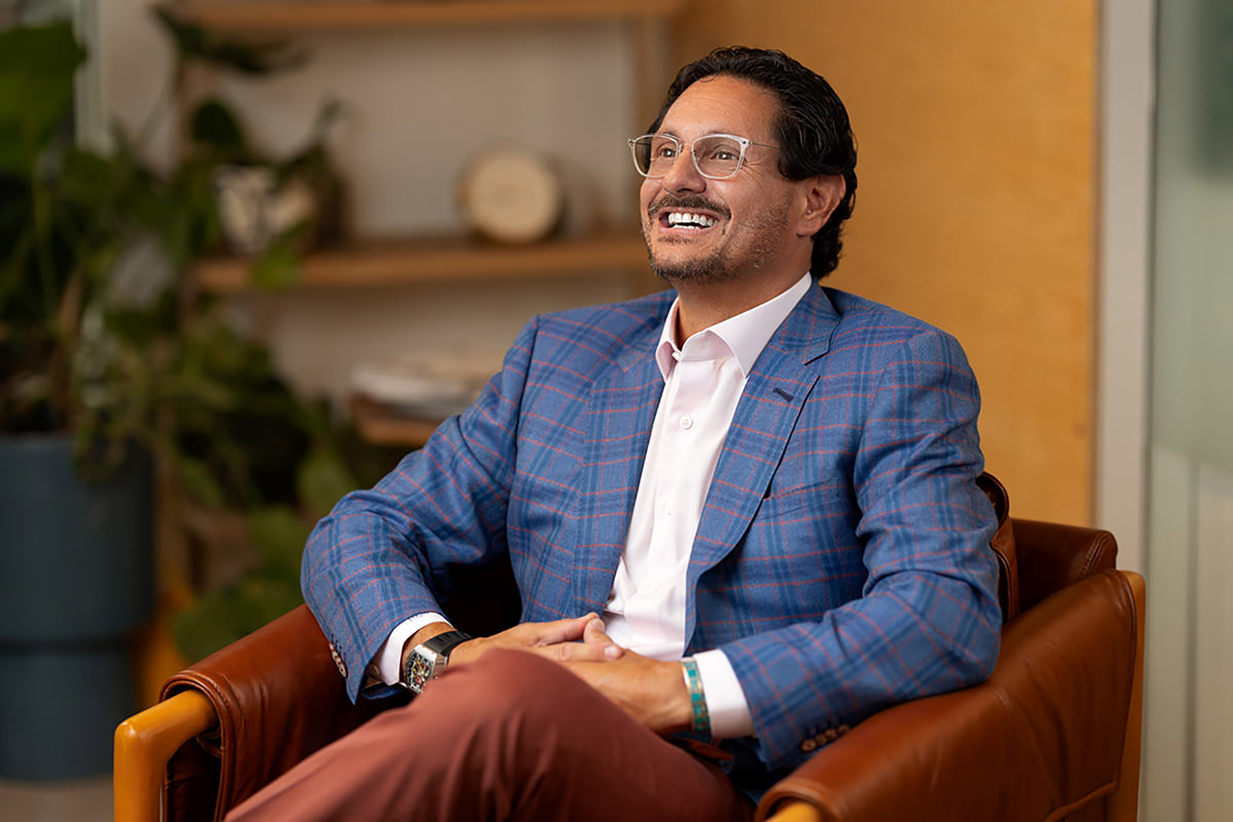 Man in a checkered suit sitting and smiling for Denver headshots in an office environment.