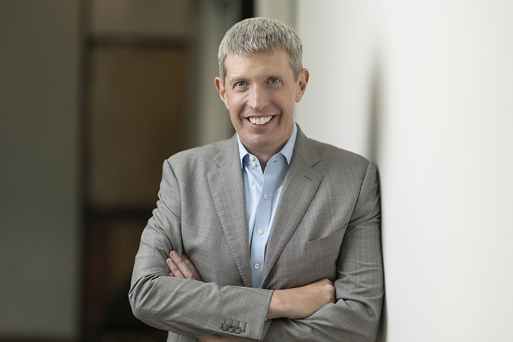 A smiling man with crossed arms wearing a gray suit and blue shirt, perfect for Denver headshots.