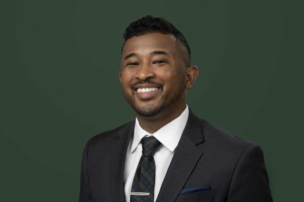A smiling man in a suit with a tie against a green background for Denver headshots.