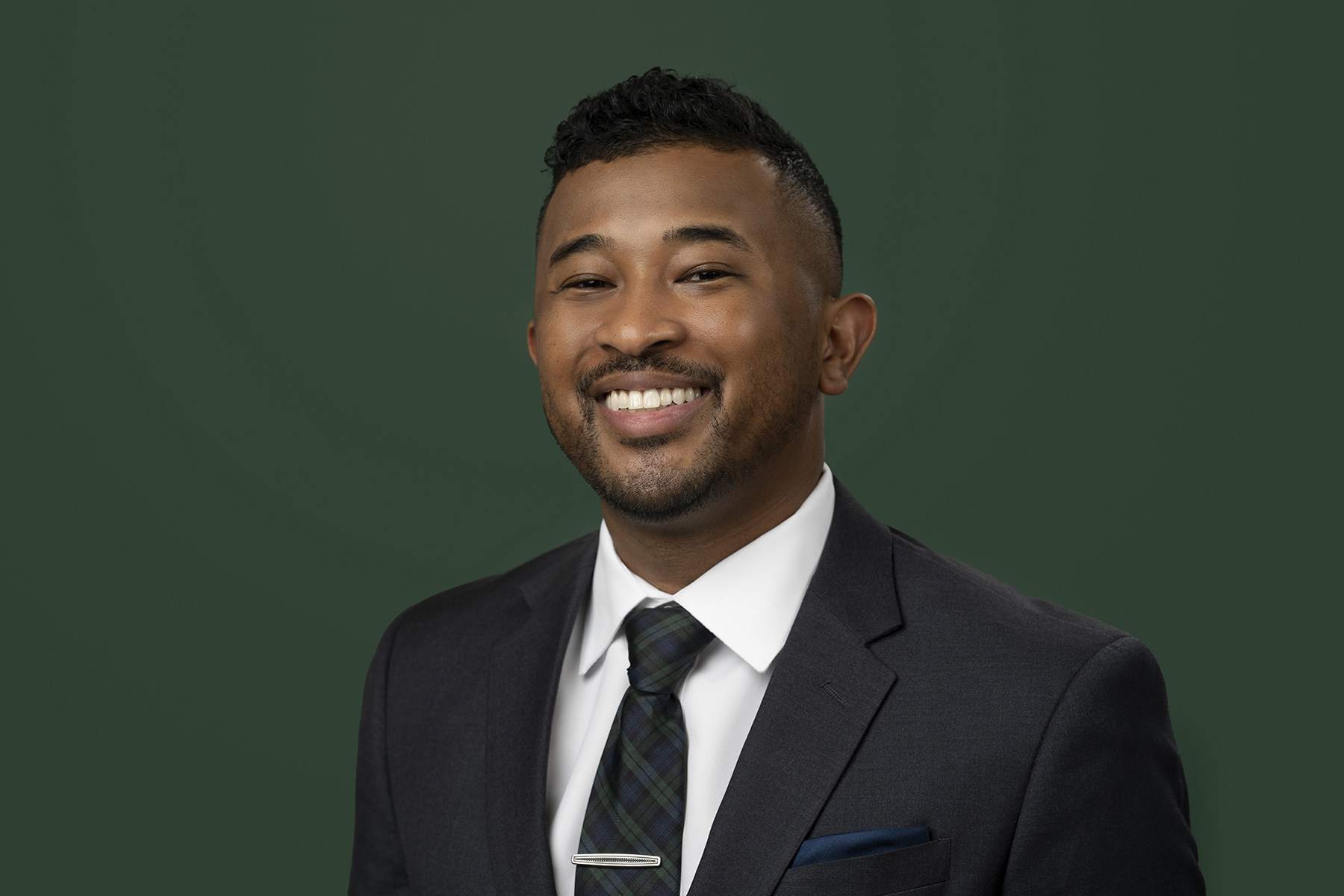 A smiling man in a suit with a tie against a green background for Denver headshots.