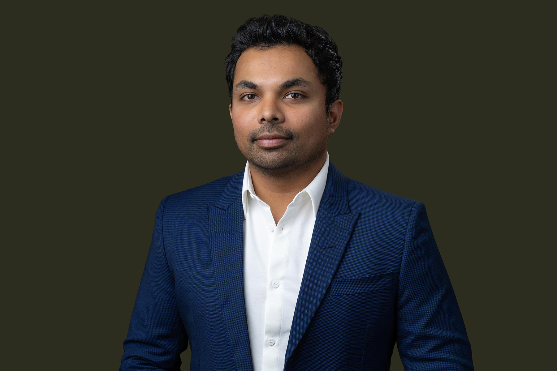 A man in a blue suit with a confident expression against a dark background poses for his Denver headshots.