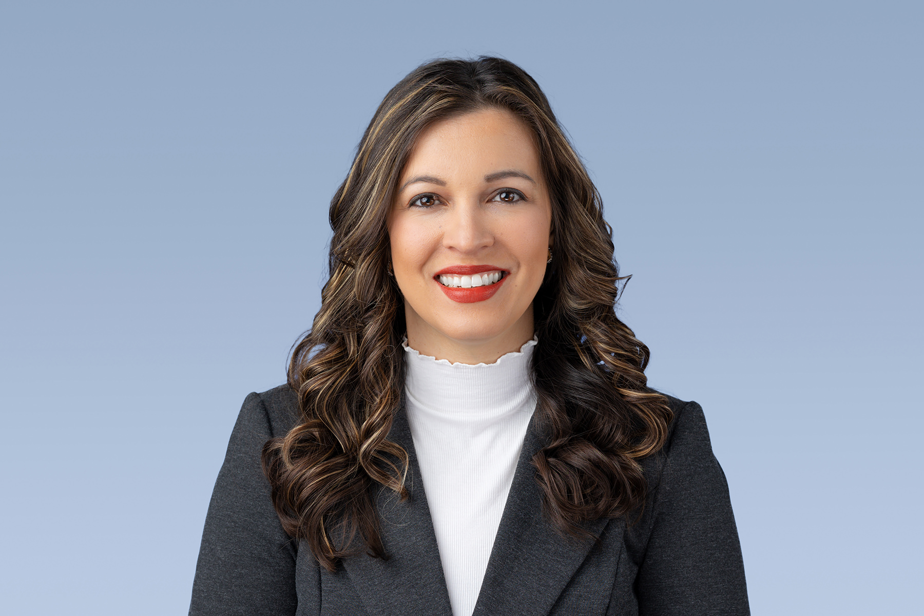 Professional woman with a friendly smile wearing a blazer and white top against a blue background for her Denver headshots.