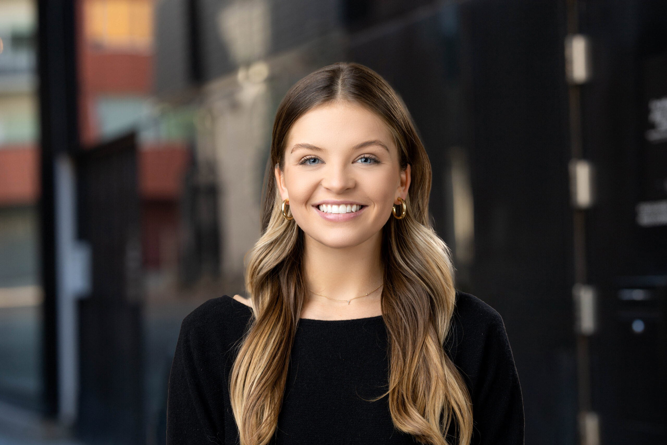 Young woman smiling in professional attire against an urban backdrop for Denver headshots.