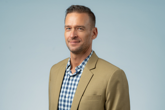 Confident man in a blazer smiling against a light blue background for his Denver headshots.