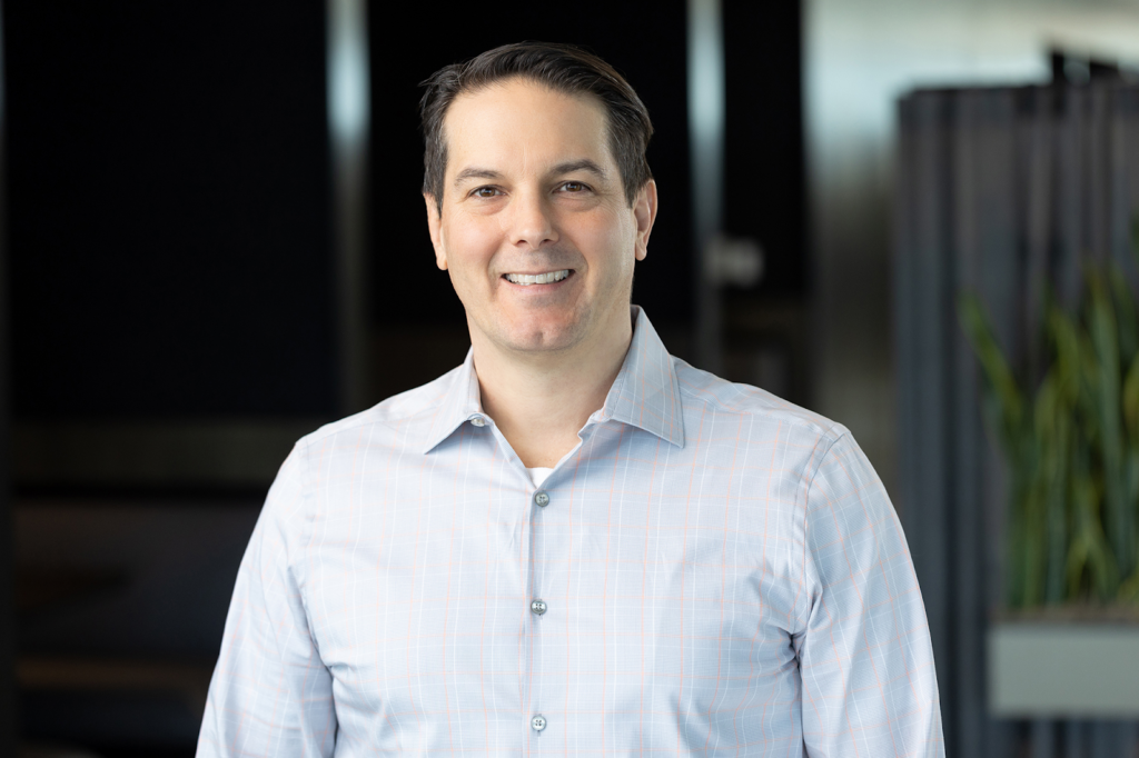 A man in a light shirt stands smiling, capturing the essence of professional individual headshots in an office environment.