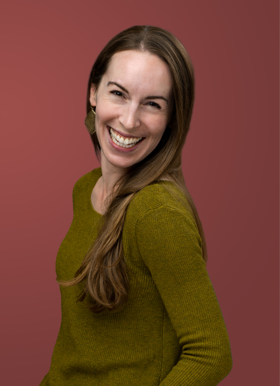 Woman with long brown hair wearing a green sweater smiles and looks at the camera, posed against a plain reddish-brown background—perfect for modern headshots or professional headshots.