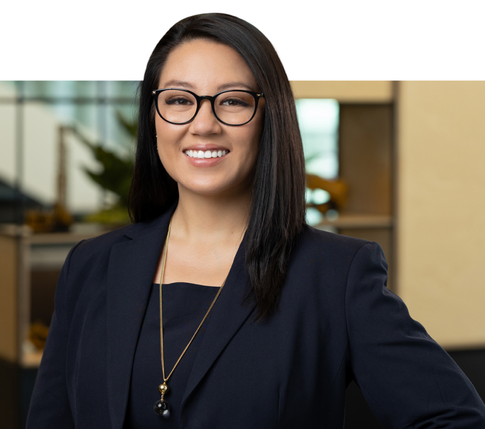 Woman with straight dark hair and glasses, smiling, wearing a navy blazer.