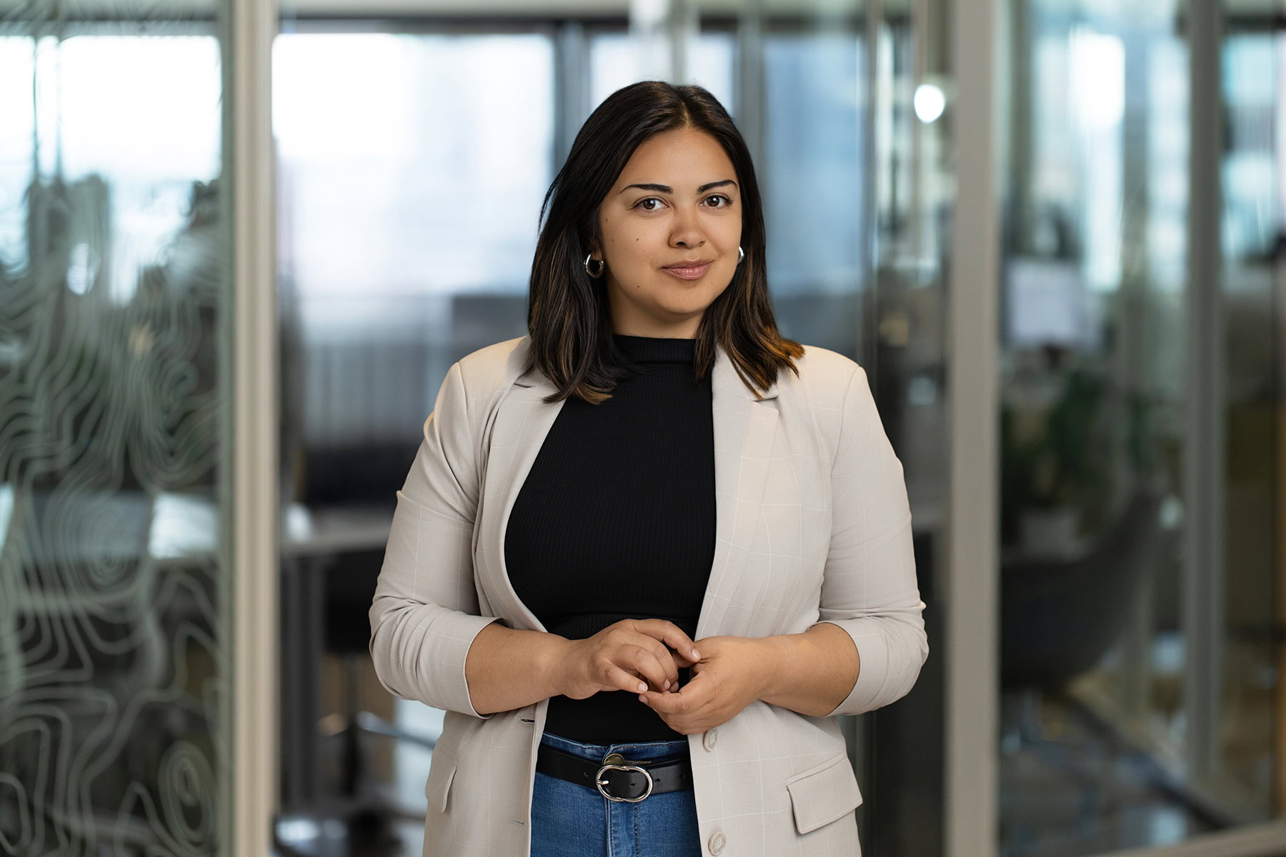 woman posing in a light tan blazer in front of a blurred office background