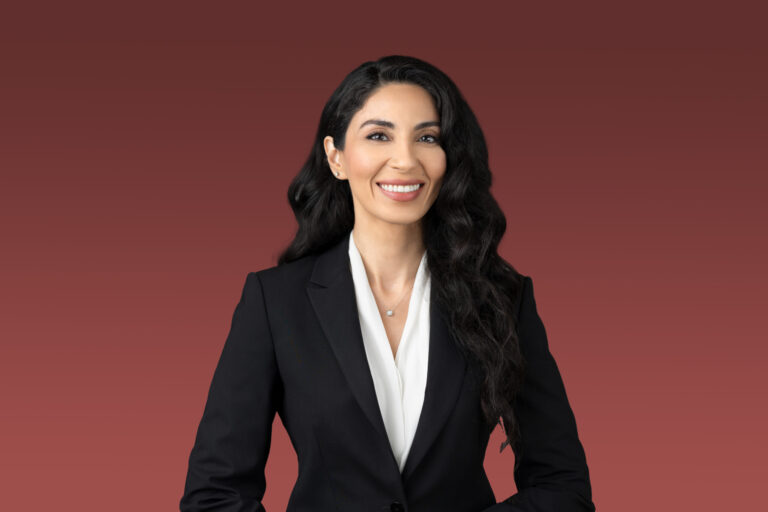Woman in a black blazer smiling on a maroon background.