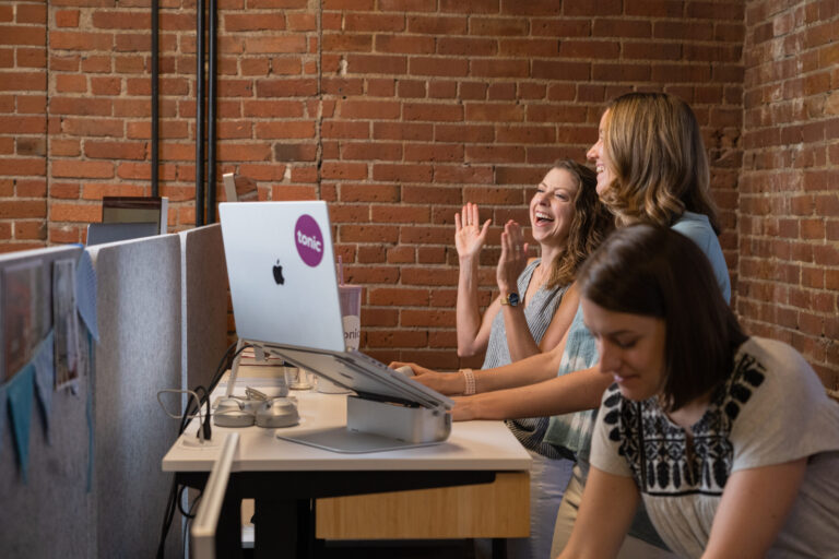 Team chatting and laughing at desks in an office.
