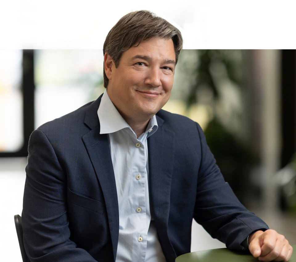 Man in a suit smiling at a table in an office.
