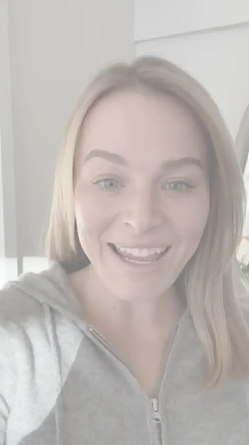 A woman with straight blonde hair smiling at the camera in a headshot, wearing a light gray zip-up hoodie indoors.